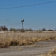 An airplane from the Austin-Bergstrom International Airport taking off just over the old Longhorn Speedway, with an infield now overgrown with grasses several feet high.